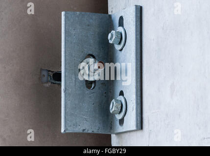 Coin métallique fixé sur un mur de ciment gris avec trois vis à vis et rondelles, avec le trou dans le mur visible. Banque D'Images