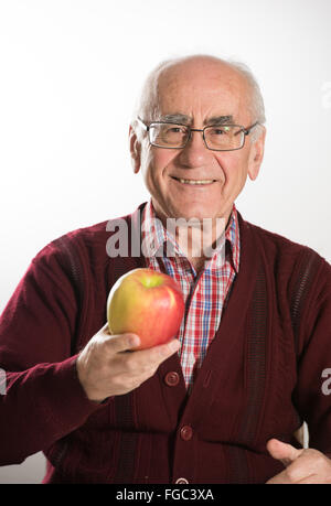 Ancien senior man holding fresh apple et souriant, portant des lunettes portant chandail rouge Banque D'Images