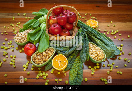 La composition des aliments santé avec des pommes dans le panier, feuilles vertes, et les écrous placés sur des tables en bois. Vue d'en haut. Banque D'Images