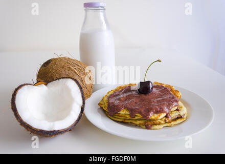 Le petit-déjeuner et le brunch repas crêpes à la noix de coco avec ouvert coco, bouteille Verre de lait et cerise sur fond blanc. Pile de Banque D'Images