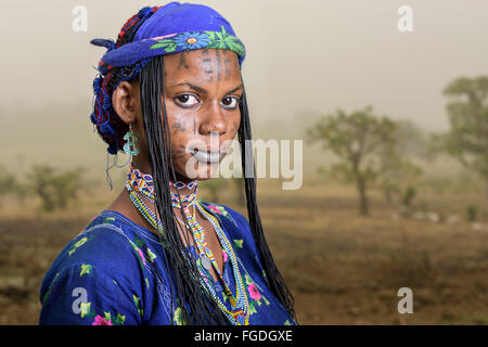 Portrait d'une femme Mbororo typique avec des cicatrices sur son visage à l'extérieur de son village pendant que l'Harmattan vent souffle la poussière. Banque D'Images