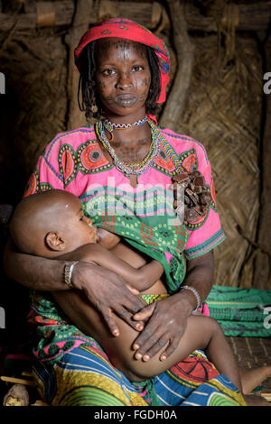 Portrait d'une femme Mbororo dans un cas typique d'une scarification sur son visage tenant son enfant à l'intérieur d'une hutte. Banque D'Images