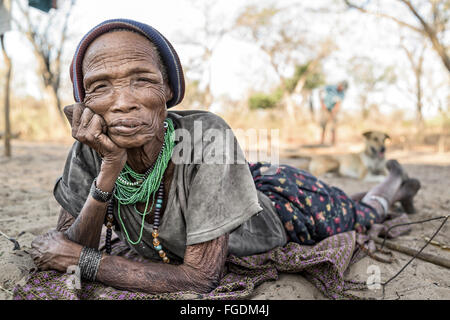 Portrait d'une femme de la tribu San étendu sur le sol de sable de son village dans une partie reculée du désert du Kalahari. Banque D'Images