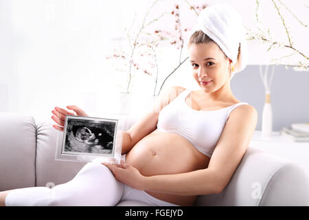 Femme enceinte bébé échographie montrant . Jeune femme enceinte échographie montre le bébé assis sur le canapé Banque D'Images