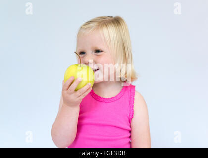 Jeune fille aux cheveux blonds holding a green apple smiling Banque D'Images