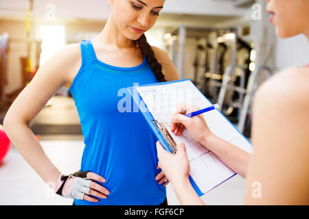 Femme avec un entraîneur personnel dans la salle de sport, un plan sur le presse-papiers Banque D'Images