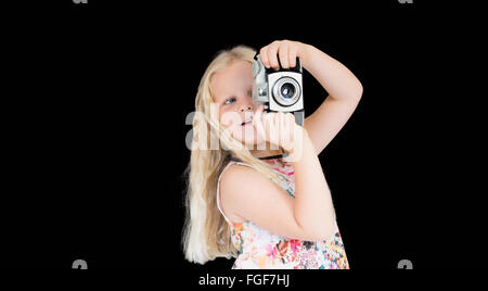 Jeune fille avec de longs cheveux blonds prendre une photographie à l'aide d'un appareil photo vintage debout sur un fond noir Banque D'Images