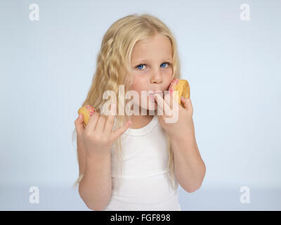 Jeune fille avec de longs cheveux blonds eating donuts et léchant ses doigts Banque D'Images