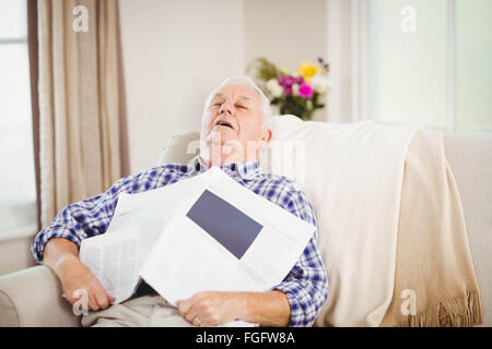 Senior man relaxing on sofa with newspaper Banque D'Images