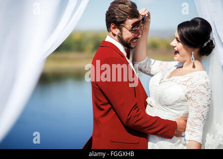 Mariée et le marié s'amuser après la cérémonie, à l'intérieur arch de nappes blanches tissu. Couleur mariage Marsala. Banque D'Images