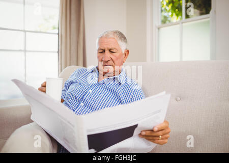 Senior man reading newspaper in living room Banque D'Images