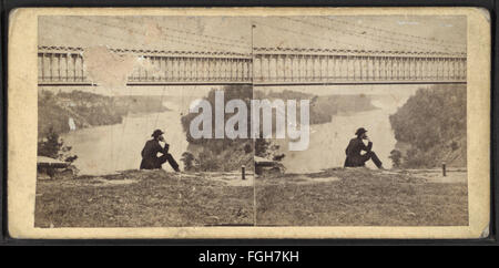 Une photographie prise sous le pont suspendu, regardant vers les chutes au loin. Capturée par E. & H.T. Anthony, cette image offre une perspective unique du monument emblématique. Banque D'Images