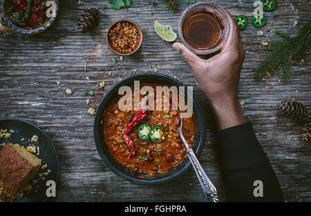 Est un homme tenant un verre rempli de bière et est sur le point de manger un bol de Turquie chili haricots surmontée de jalapenos et un temps chaud et sec serran Banque D'Images