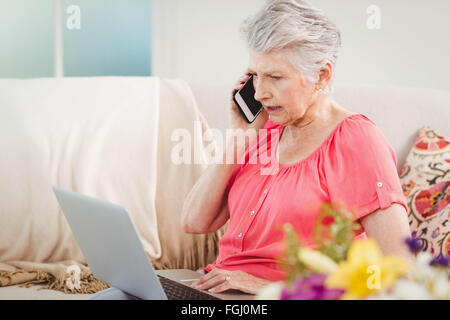 Senior Woman talking on phone and using laptop Banque D'Images