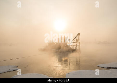 Un remorqueur bateau dans la brume au coucher du soleil d'hiver Banque D'Images