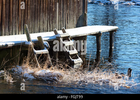 Deux petites marches en bois d'un pont de pêche et baignade dans l'eau glacée à côté d'un hangar à bateaux en hiver. Quelques vegetat Banque D'Images