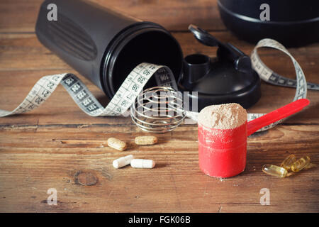 La poudre de protéine de lactalbumine en écope de vitamines et de plastique shaker sur fond de bois. Banque D'Images