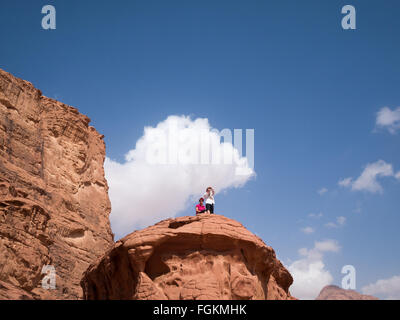 Les touristes à la recherche à l'échelle du paysage en haut d'un rocher dans le Wadi Rum Banque D'Images