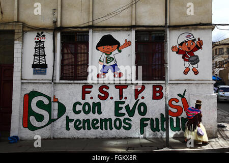 La Paz, Bolivie, 20 février 2016. Une femme aymara ou une cholita vêtue de vêtements traditionnels passe devant une murale de campagne montrant son soutien à l'actuel président bolivien Evo Morales (représenté comme un jeune garçon sur la murale). Le 21 février, la Bolivie vote par référendum pour approuver ou rejeter une modification de l'article 168 de la Constitution. Un vote Oui permettrait au président et au vice-président de se présenter pour plus d’un mandat consécutif, ce qui signifie qu’Evo Morales pourrait se présenter à nouveau comme candidat aux élections de 2019 (il ne peut pas selon la constitution actuelle). Crédit : James Brunker / Alamy Live News Banque D'Images