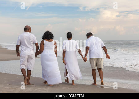 Happy senior African American les hommes et les femmes des couples marchant main dans la main sur une plage tropicale déserte Banque D'Images