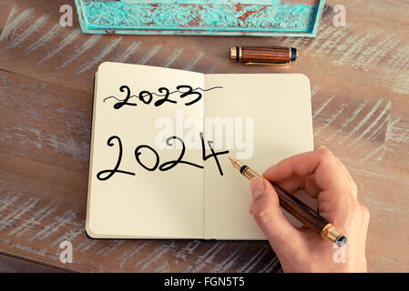 Effet rétro aux couleurs et image d'une femme d'écrire une note à la main avec un stylo sur un ordinateur portable. Concept de motivation avec texte manuscrit Bonne année 2024 et 2023 written off Banque D'Images