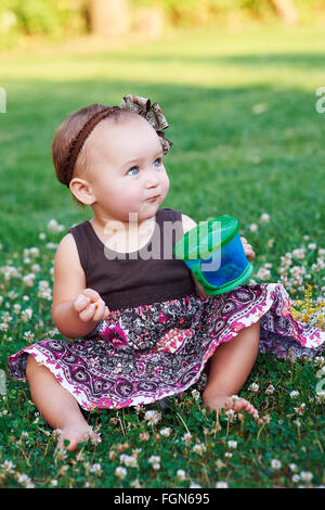 Petite fille assise sur l'herbe avec un mug Banque D'Images