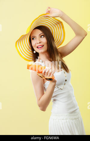 Vacances été la mode. et concept de soins de la peau. Femme au chapeau jaune en forme de cœur contient lotion solaire, lunettes arrière-plan lumineux copy space Banque D'Images