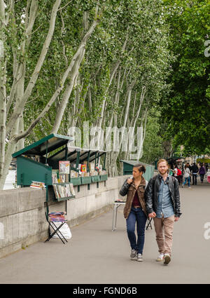 Un couple marche par livre-stands qu'une ligne de la rue Paris, à côté de la rivière Seine Banque D'Images