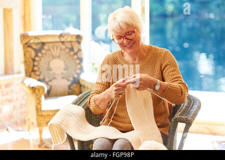 Senior woman knitting in living room Banque D'Images