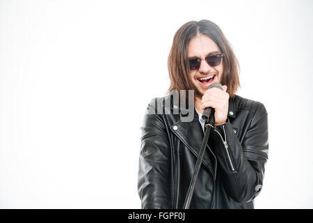 Beau jeune chanteur rock en veste en cuir noire et lunettes de chanter dans le micro sur fond blanc Banque D'Images