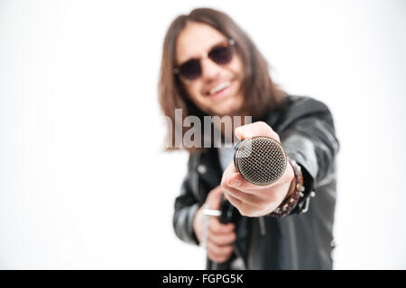 Joyeux jeune homme aux cheveux longs en donnant des lunettes d'un microphone et vous offrant à chanter sur fond blanc Banque D'Images