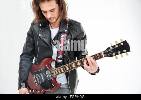 Beau jeune homme aux cheveux longs en veste en cuir noire playing electric guitar over white background Banque D'Images