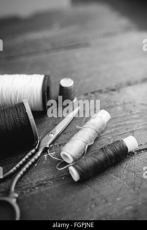 Accessoires de couture : bobines de fil, ciseaux, aiguilles, dé sur table en bois. Photo en noir et blanc. La couture et la couture concept. Banque D'Images