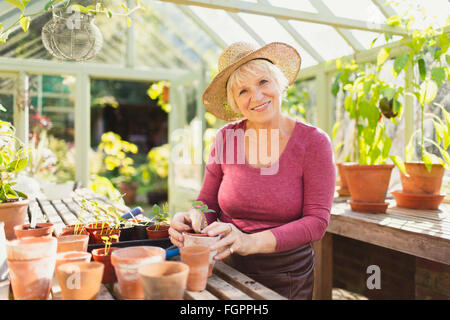 Portrait of smiling senior woman potting plants in greenhouse Banque D'Images