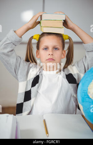 Cute élève balancing books on head in a classroom Banque D'Images