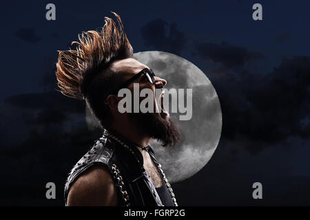 Jeune homme avec un Mohawk hairstyle crier dans la nuit en face de la pleine lune Banque D'Images