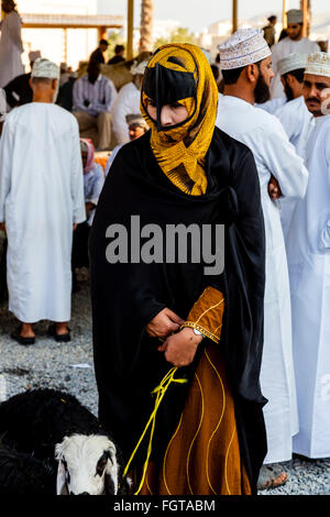 Un Omanais femme vêtue de la Traditionnelle Costume Omaniya au marché de l'élevage Vendredi à Nizwa, Al Dakhiliyah, Région de l'Oman Banque D'Images