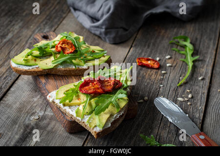 Toast avec du fromage de chèvre en bonne santé, d'avocat, roquette et tomates séchées au soleil sur une table en bois rustique. Selective focus Banque D'Images