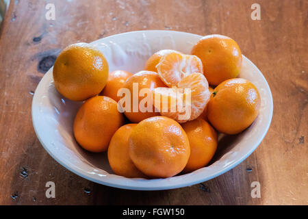 Mandarines, Citrus reticulata, avec un pelé, dans un bol blanc. Banque D'Images