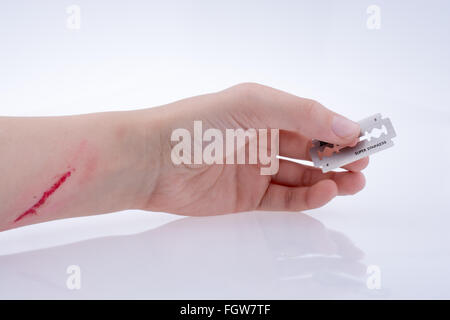 Main blessée tenant une lame de rasoir sur fond blanc Banque D'Images