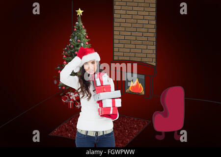 Composite image of brunnette in santa hat holding gifts Banque D'Images