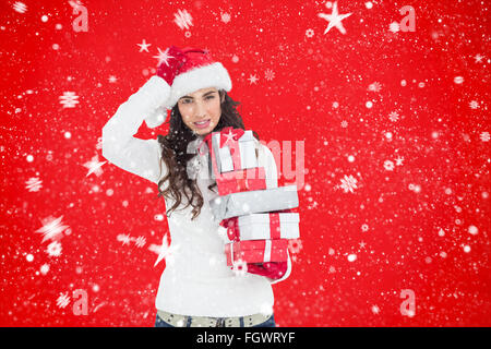 Composite image of brunnette in santa hat holding gifts Banque D'Images