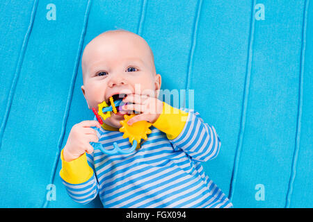 Mignon bébé tricoté bleu sur une couverture. La dentition à jouer avec des jouets colorés. Petit garçon au lit après pan. Banque D'Images