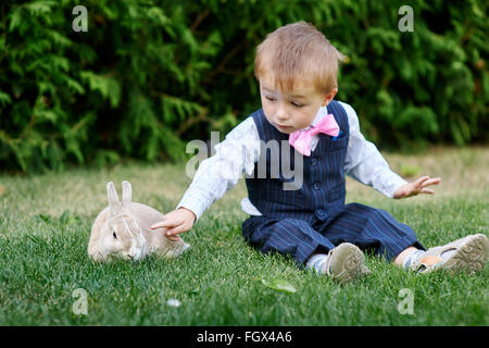 Petit garçon dans un costume de jouer avec un lapin sur l'herbe Banque D'Images