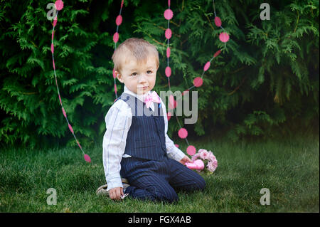 Petit garçon dans un costume avec un bouquet assis sur l'herbe Banque D'Images