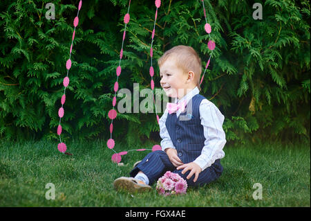 Petit garçon dans un costume avec un bouquet assis sur l'herbe Banque D'Images