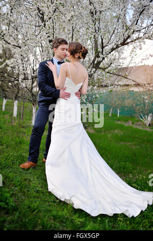 Mariée et le marié qui englobe dans un jardin de printemps en fleurs Banque D'Images