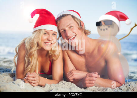 Image composite du couple lying on beach portant des chapeaux de Noël Banque D'Images