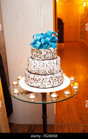 Beau blanc gâteau à trois niveaux avec un arc turquoise sur le dessus est sur la table Banque D'Images