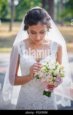 Mariée en robe blanche en été parc verdoyant avec un bouquet dans la main Banque D'Images